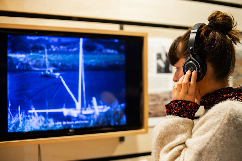 Un visiteur regarde un film d'archives dans l'exposition Rivages partagés.